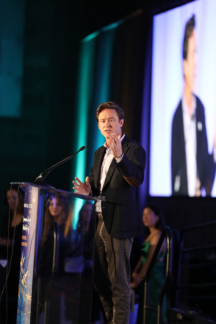 Speaker addressing an audience at a gala beneath colorful stage lights